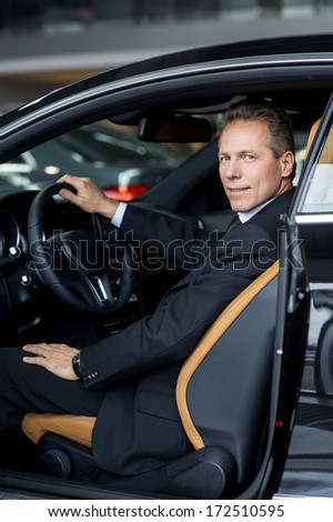 I love my new car. Side view of confident senior man in formalwear sitting in car and smiling at camera