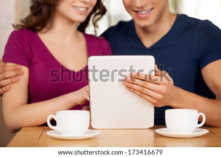 Surfing the net together. Cropped image of beautiful young loving couple sitting at the restaurant and using digital tablet