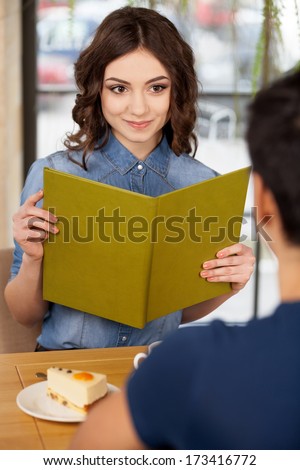 Couple at restaurant. Beautiful young couple sitting together at the restaurant while woman holding menu and smiling