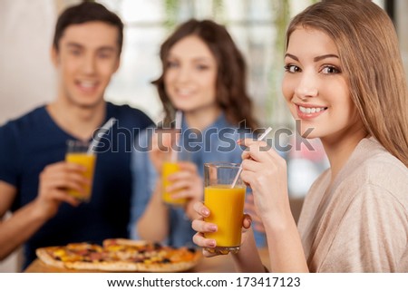 Friends at the restaurant. Three cheerful young people eating pizza at the restaurant while beautiful woman looking over shoulder and smiling