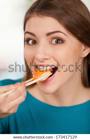 Nigiri is my favorite. Beautiful young woman eating sushi and smiling while sitting at the restaurant