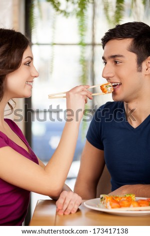 Couple eating sushi. Beautiful young couple sitting together at the restaurant while woman feeding her boyfriend with sushi