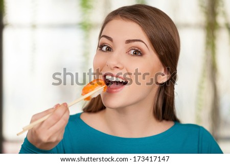 Addicted to sushi. Beautiful young woman eating sushi and smiling while sitting at the restaurant