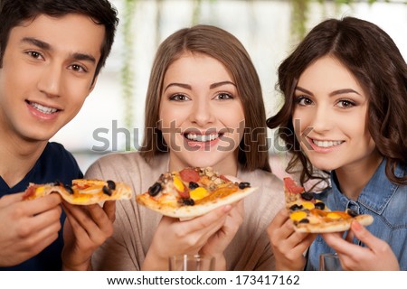 Eating A Fresh Pizza. Three Cheerful Young People Eating Pizza And Smiling At Camera