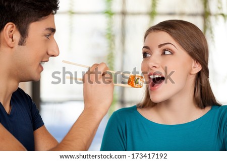 Couple eating sushi. Beautiful young couple sitting together at the restaurant while man feeding his girlfriend with sushi