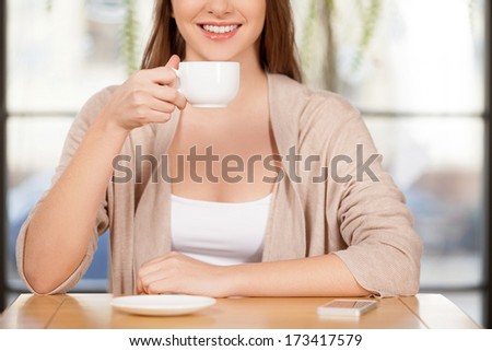 Drinking a fresh coffee. Cropped image of beautiful young woman drinking coffee at the restaurant and smiling at camera