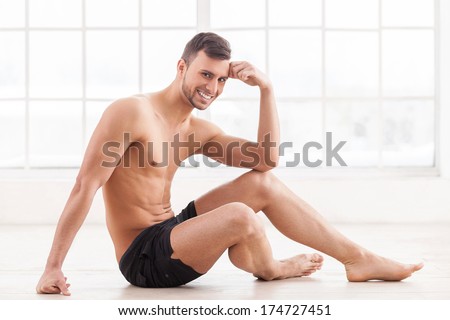Keeping body in perfect shape. Handsome young muscular man sitting on the floor and smiling