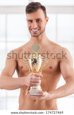 Real achievement. Handsome young muscular man holding a golden trophy in his hands and smiling