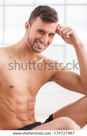 Strong and confident. Handsome young muscular man smiling at camera and holding head in hand