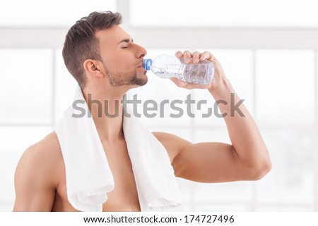 Drinking water after workout. Handsome young muscular man with towel on shoulders drinking water and keeping eyes closed