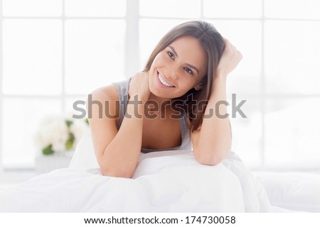 Day dreaming in bed. Cheerful young smiling woman relaxing in bed and looking away