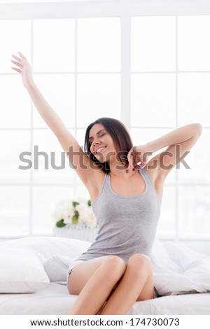 Morning stretching. Beautiful young smiling woman sitting in bed and stretching out