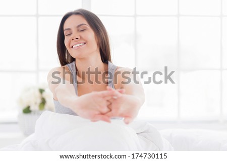Starting a day from stretching. Beautiful young smiling woman stretching out in bed and keeping eyes closed