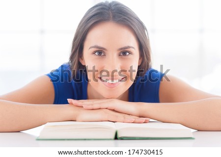 It is my favorite book! Beautiful young woman leaning at the table with book laying on it and smiling
