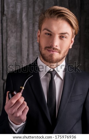 Man with a smoking pipe. Portrait of handsome young man in formalwear holding a smoking pipe and smiling at camera