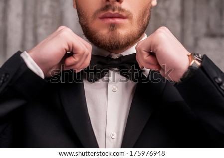 Tying a bow tie. Cropped image of handsome young beard man in formalwear adjusting his bow tie