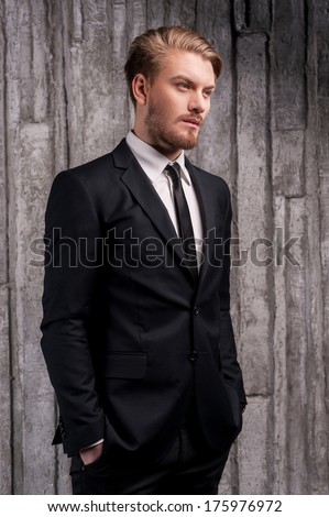 Stylish handsome. Side view of handsome young man in formalwear holding hands in pockets and looking away