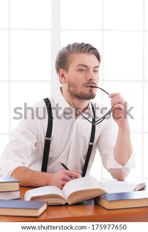 Waiting for inspiration. Thoughtful young man in shirt and suspenders holding glasses and looking away while sitting at his working place