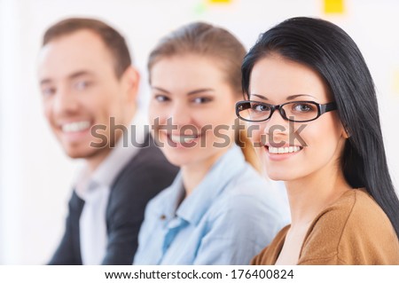 Strong business team. Three cheerful young colleagues sitting together at their working place and smiling at camera