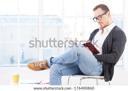 Handsome bookworm. Thoughtful young man in shirt sitting on the chair and reading a book