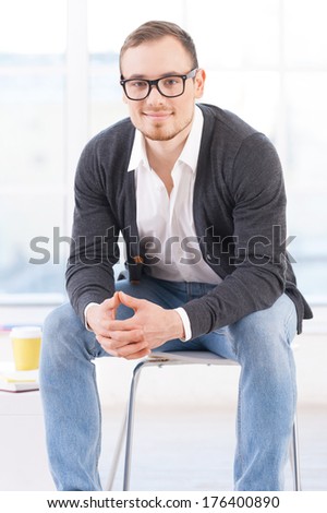 Looking for inspiration. Thoughtful young man in shirt looking at camera and smiling while sitting on the chair