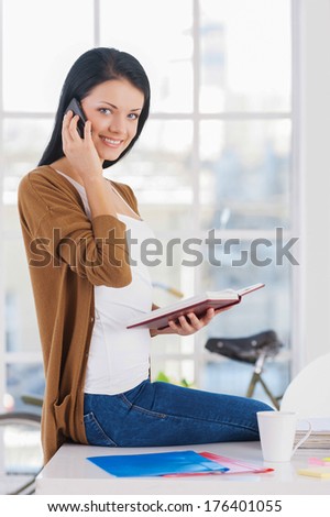 She is always in touch. Cheerful young businesswoman in casual wear talking on the phone and smiling