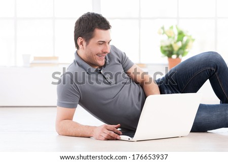 Surfing the net at home. Cheerful young man lying on the floor and using computer