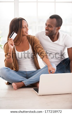 Working at their new tablet. Beautiful young African couple using digital tablet while sitting together on the floor at their apartments