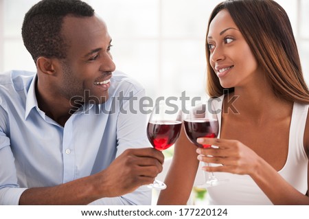 Today is their special date. Beautiful young African couple sitting close to each other and holding wineglasses
