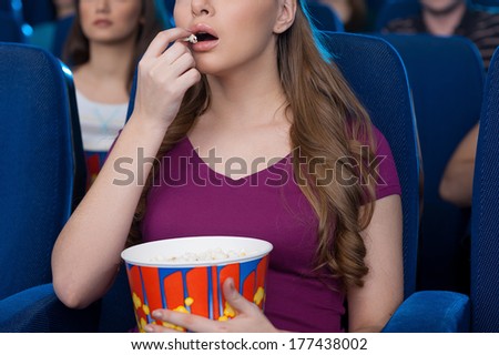 Eating popcorn at the cinema. Cropped image of beautiful young woman eating popcorn and watching movie while sitting at the cinema