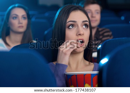Woman at the cinema. Attractive young woman eating popcorn and watching movie while sitting at the cinema