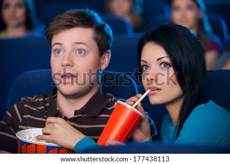 This movie is so exciting! Excited young couple eating popcorn and drinking soda while watching movie at the cinema