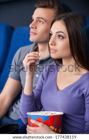 What an exciting movie! Excited young couple eating popcorn while watching movie at the cinema