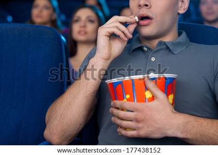 Man eating popcorn at the cinema. Cropped image of young man eating popcorn and watching movie while sitting at the cinema