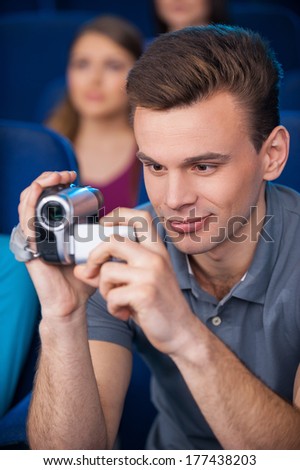 Man pirating at the cinema. Young man shooting with his home video camera while sitting at the cinema