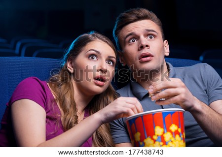 This movie is so scary! Shocked young couple eating popcorn and watching movie together while sitting at the cinema
