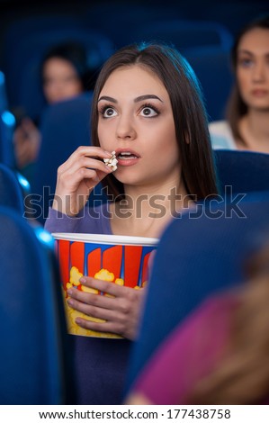 Amazing movie! Excited young woman eating popcorn and watching movie while sitting at the cinema