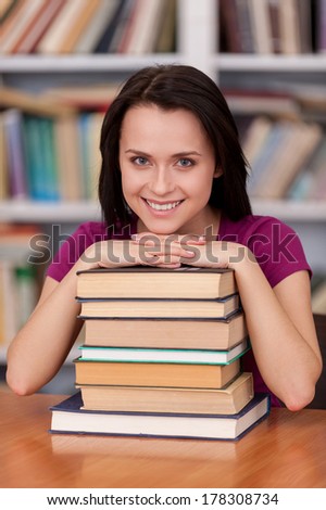 Feeling confident before her final exams. Cheerful young female student holding books and smiling while standing at the library