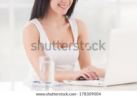 Beautiful business lady at work. Cropped image of beautiful young woman working on laptop and smiling while sitting at the table