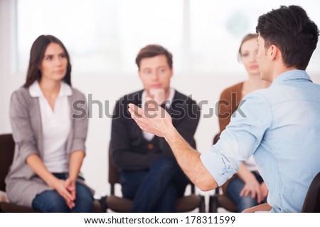 Sharing his problems with people. view of man telling something and gesturing while group of people sitting in front of him and listening