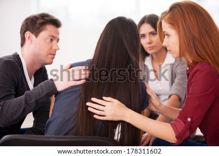 We understand you. Rear view of depressed young woman sitting at the chair while other people comforting her