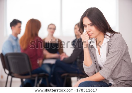 Feeling lonely and depressed. Depressed young woman sitting at the chair and crying while other people communicating on background