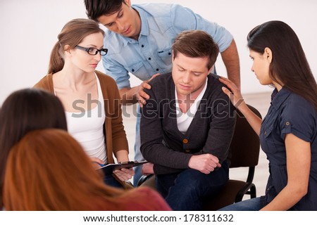 Be strong! Top view of depressed young man sitting at the chair while other people comforting him