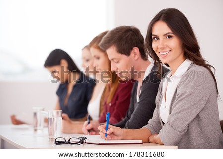 People at the seminar. Attractive young woman smiling at camera while sitting together with another people at the table