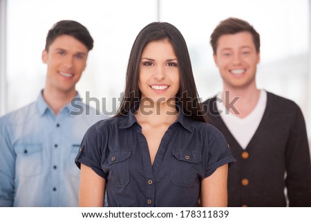 Real leader. Attractive young woman smiling while two men standing behind her