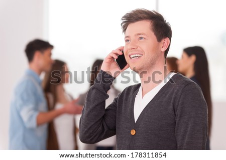 Team leader on the phone. Handsome young man talking on the mobile phone and smiling while group of people communicating on background