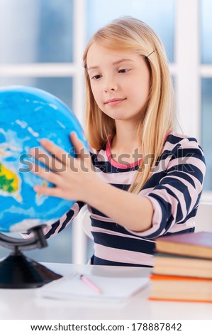 Examining globe. Cheerful little girl examining globe while sitting at the table