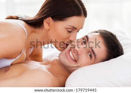 I love her! Beautiful young loving couple lying in bed while woman kissing her boyfriend at cheek