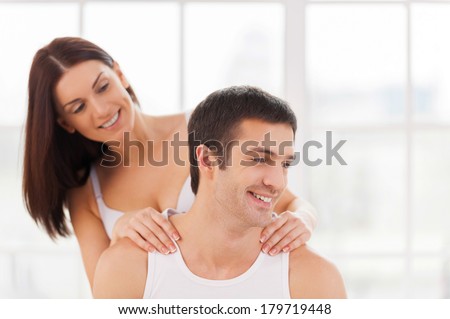 Enjoying massage. Beautiful young loving couple sitting together in bed while woman doing massage toi her boyfriend