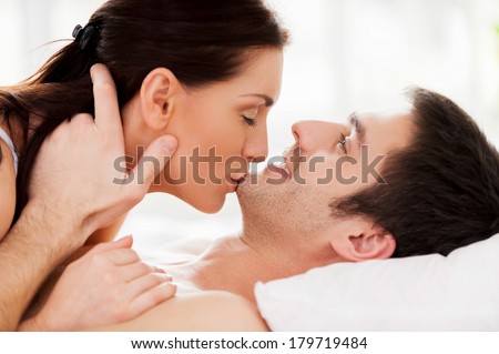 Sensual moments. Beautiful young loving couple lying in bed while woman kissing her boyfriend chin
